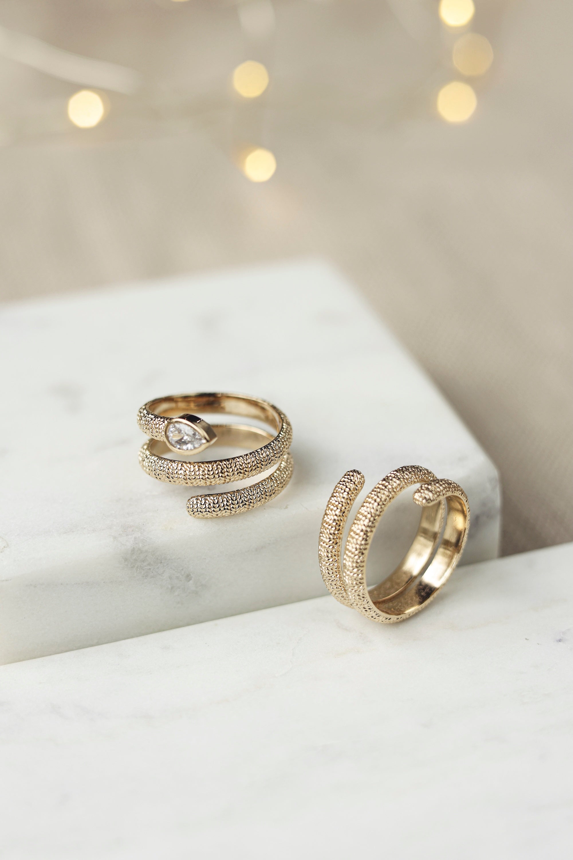 Bague dorée Abi zircon en spirale texturée ornée d'un zircon - Bijou photographié sur un présentoir en marbre blanc