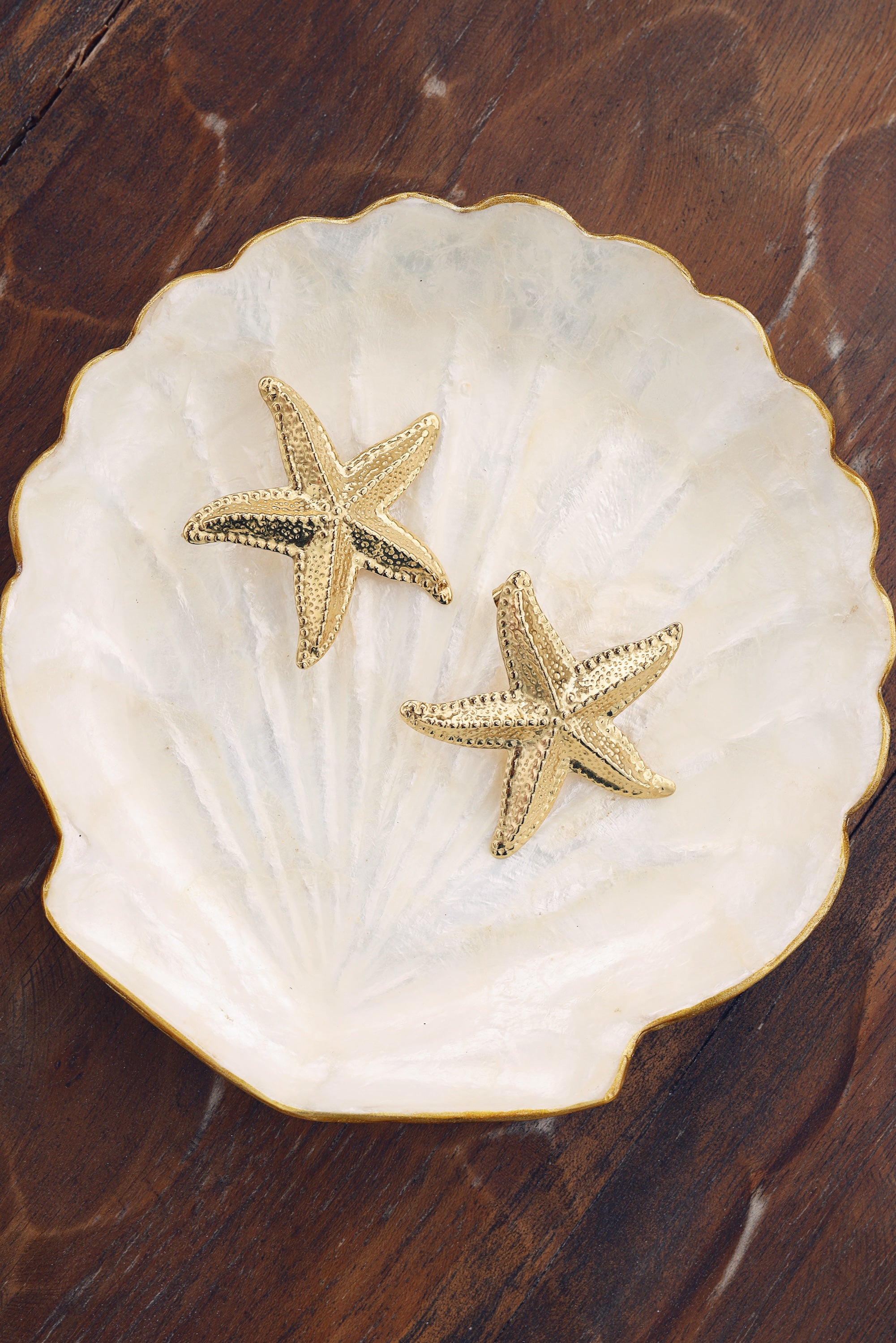 Boucles d'oreilles dorées Mirah étoile de mer - Bijou photographié sur coupole coquillage en nacre avec bordure dorée