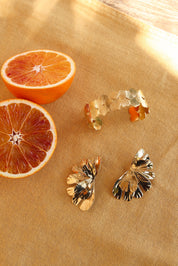 Boucles d'oreilles dorées Alga - Bijou photographié sur tissu jaune avec oranges sanguines