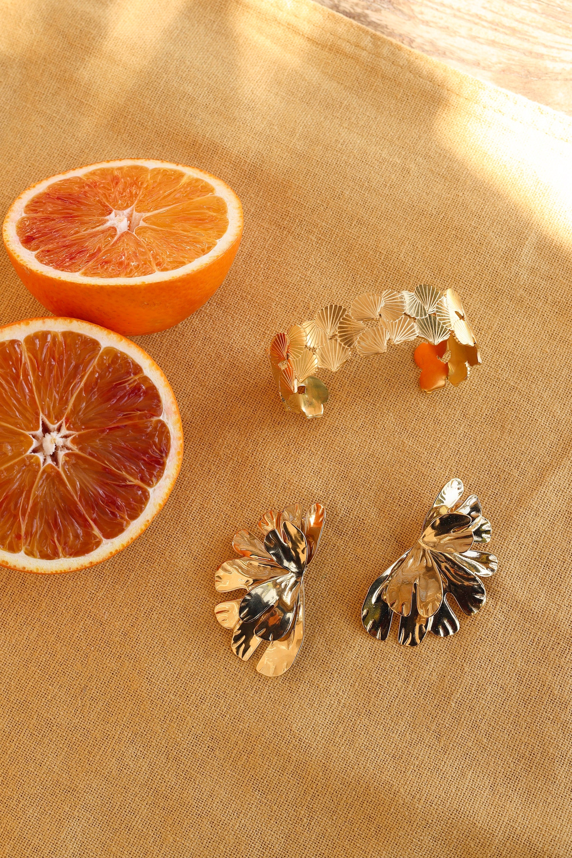 Boucles d'oreilles dorées Alga - Bijou photographié sur tissu jaune avec oranges sanguines