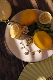 Boucles d'oreilles Larysa dorées coquillage - Bijou photographié sur assiette blanche avec citrons et collier perles en nacre et pendentifs
