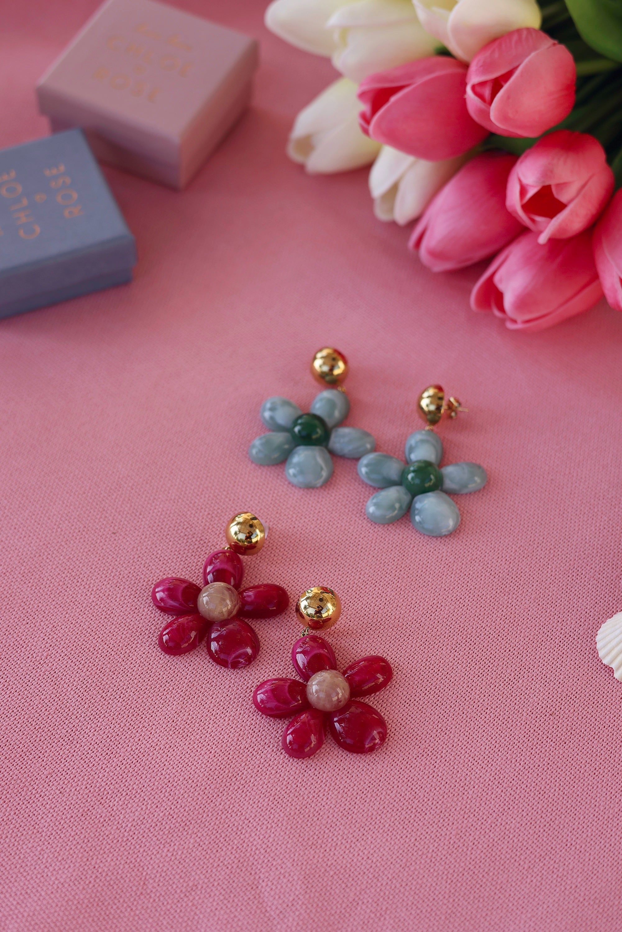 Boucles d'oreilles pendantes dorées Marty vert en acétate - Bijou photographié sur tissu rose avec tulipes et boites cadeau Chloe Rose