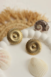 Boucles d'oreilles puces dorées Eunice en forme de spirale - Bijou photographié dans un décor estival