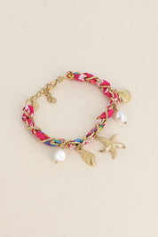 Bracelet doré Aminata fuchsia maille entrelacée avec tissu rose fuchsia pendentifs coquillages, étoile de mer et nacres - Bijou photographié sur fond beige
