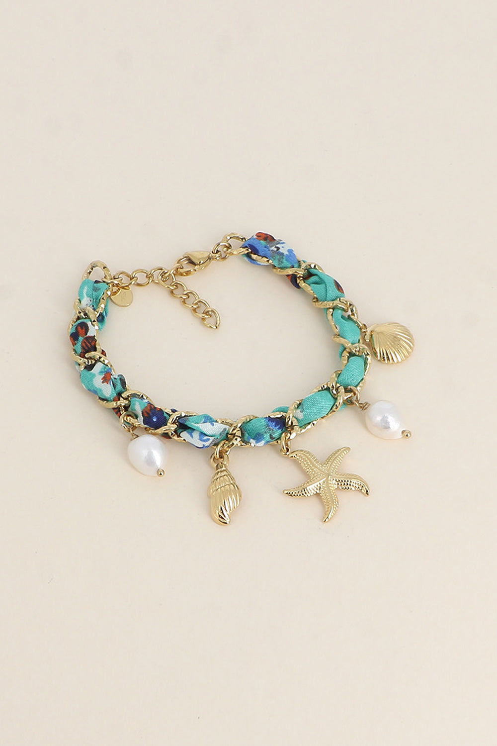 Bracelet doré Aminata maille entrelacée avec tissu turquoise pendentifs coquillages, étoile de mer et nacres - Bijou photographié sur fond beige
