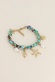 Bracelet doré Aminata maille entrelacée avec tissu turquoise pendentifs coquillages, étoile de mer et nacres - Bijou photographié sur fond beige
