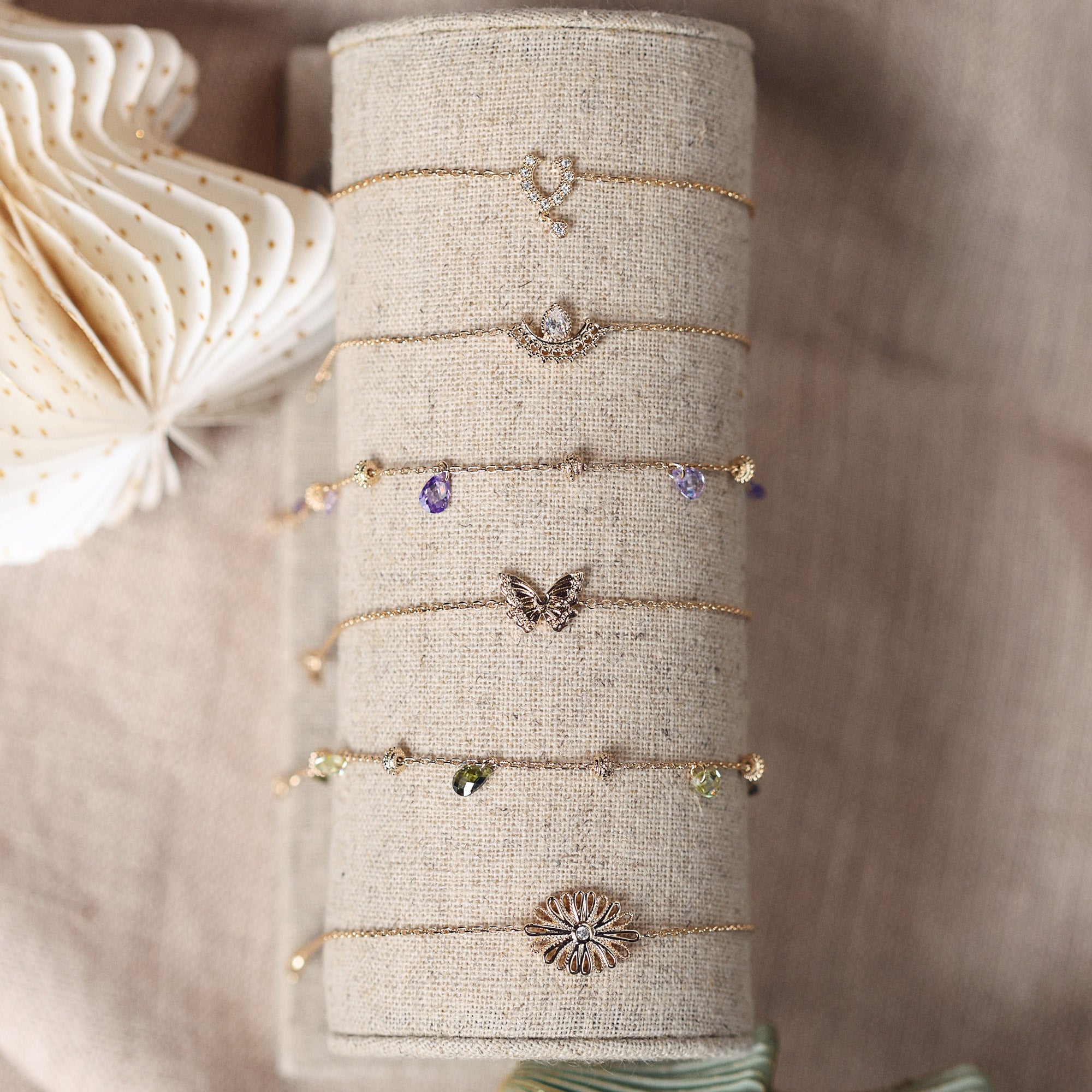 Bracelet Shaan en plaqué or avec un charm en forme de fleur et un zircon au centre, bijou délicat et raffiné - Bijou photographié sur présentoir en lin