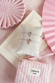 Bracelet personnalisable en argent Kaïs anneau avec nœud orné de zircons pour lettres de l'alphabet et charms - Bijou photographié sur un coussin avec des décorations roses