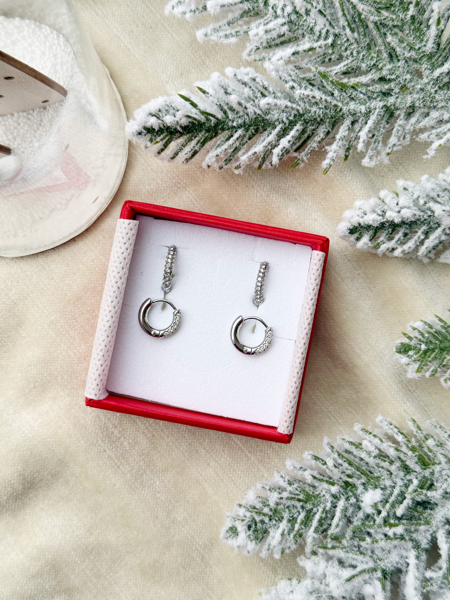 Coffret de parure de bijoux Divine contenant deux paires de mini créoles argentées ornées de zircons - Bijoux photographié dans un écrin à bijoux rouge dans une ambiance de Noël