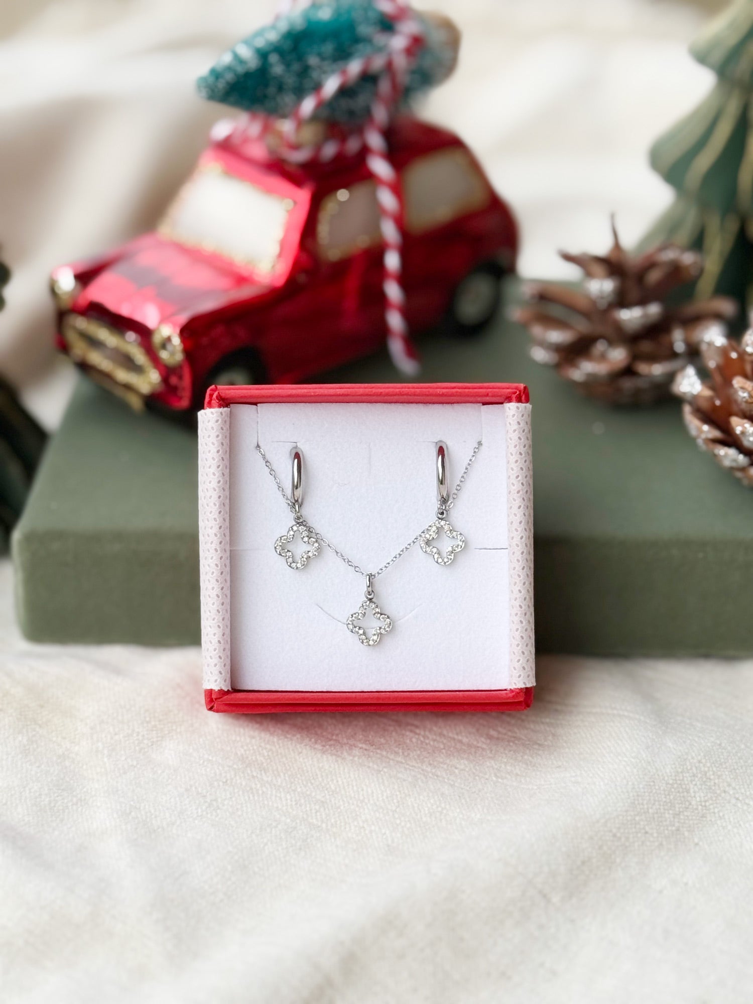Coffret de parure Lovely comprenant une paire de mini créoles et un collier argentés, ornés d’un pendentif trèfle serti de zircons - Bijoux photographiés dans un écrin à bijoux rouge dans une ambiance de Noël