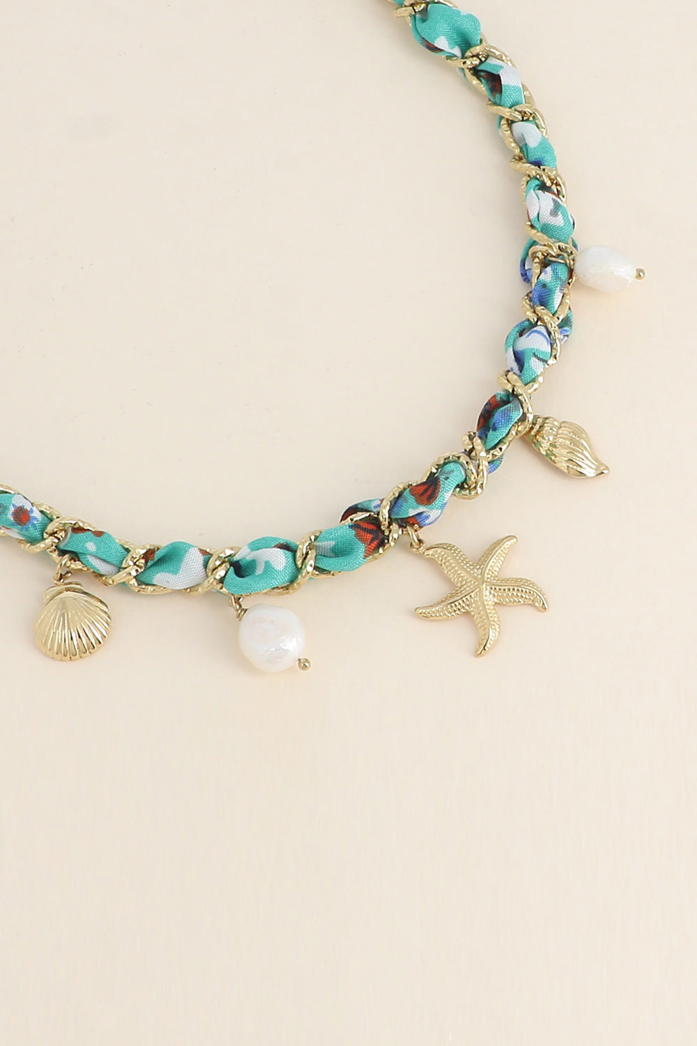 Collier doré Aminata maille entrelacée avec tissu turquoise pendentifs coquillages, étoile de mer et nacres - Bijou photographié sur fond beige
