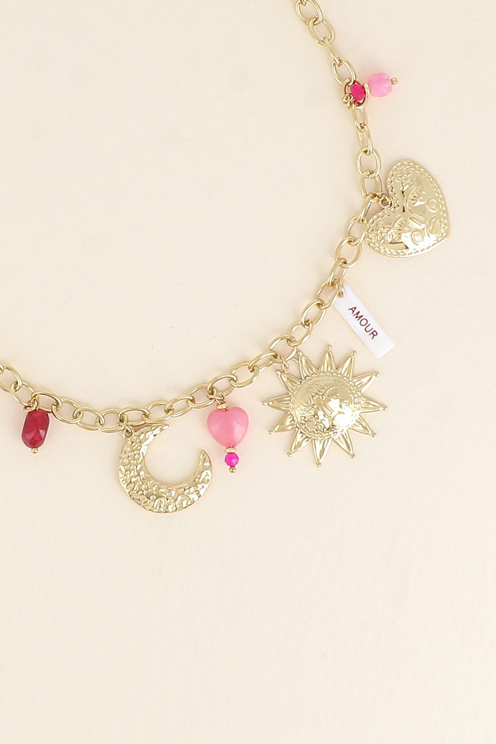 Collier maille doré Solal pendentifs soleil, cœur, Lune, pierres naturelles et amulette en nacre avec inscription "amour" - Bijou photographié sur fond beige