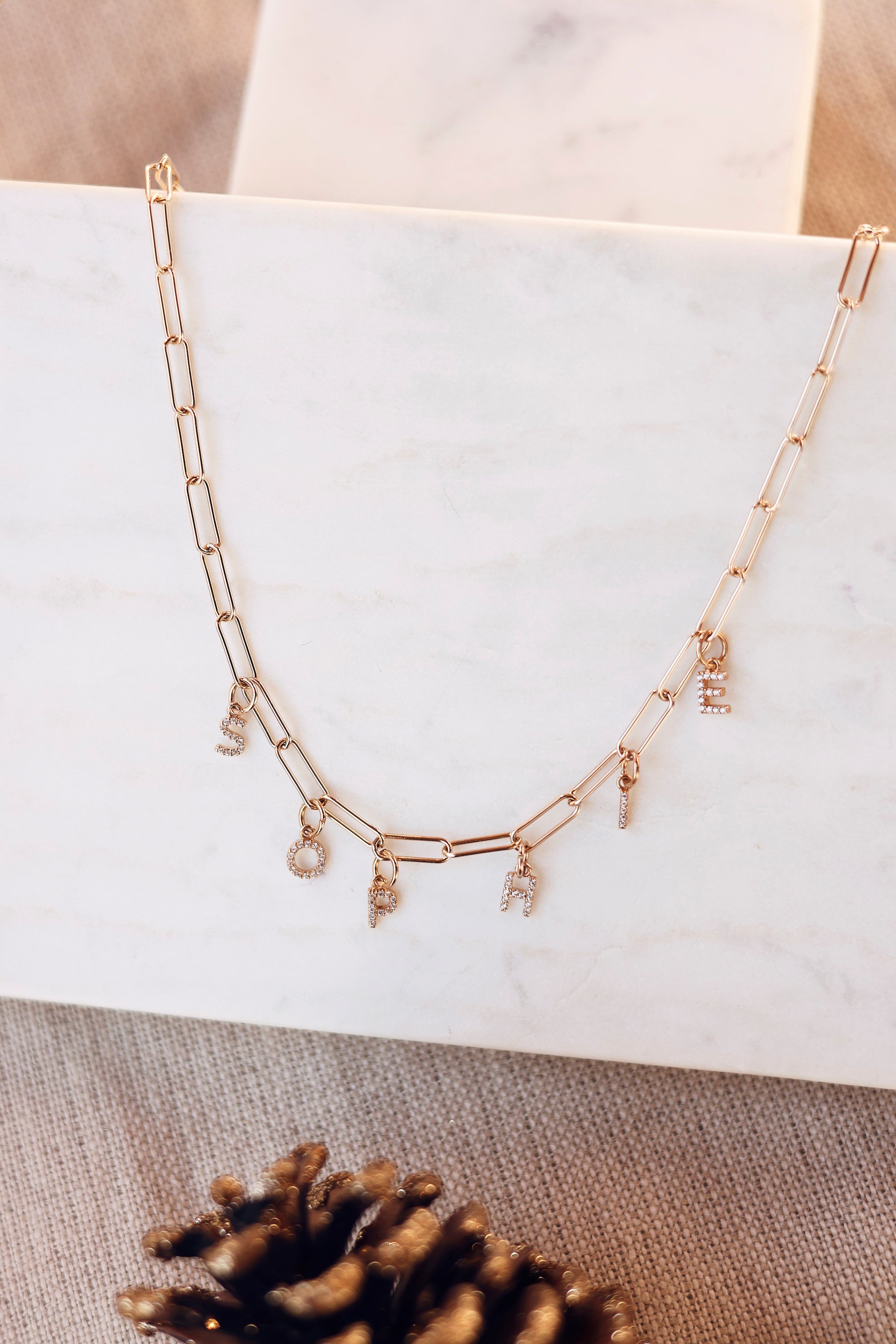 Collier personnalisable doré Axelle maille pour lettres de l'alphabet et charms - Bijou photographié sur une planche en marbre blanc