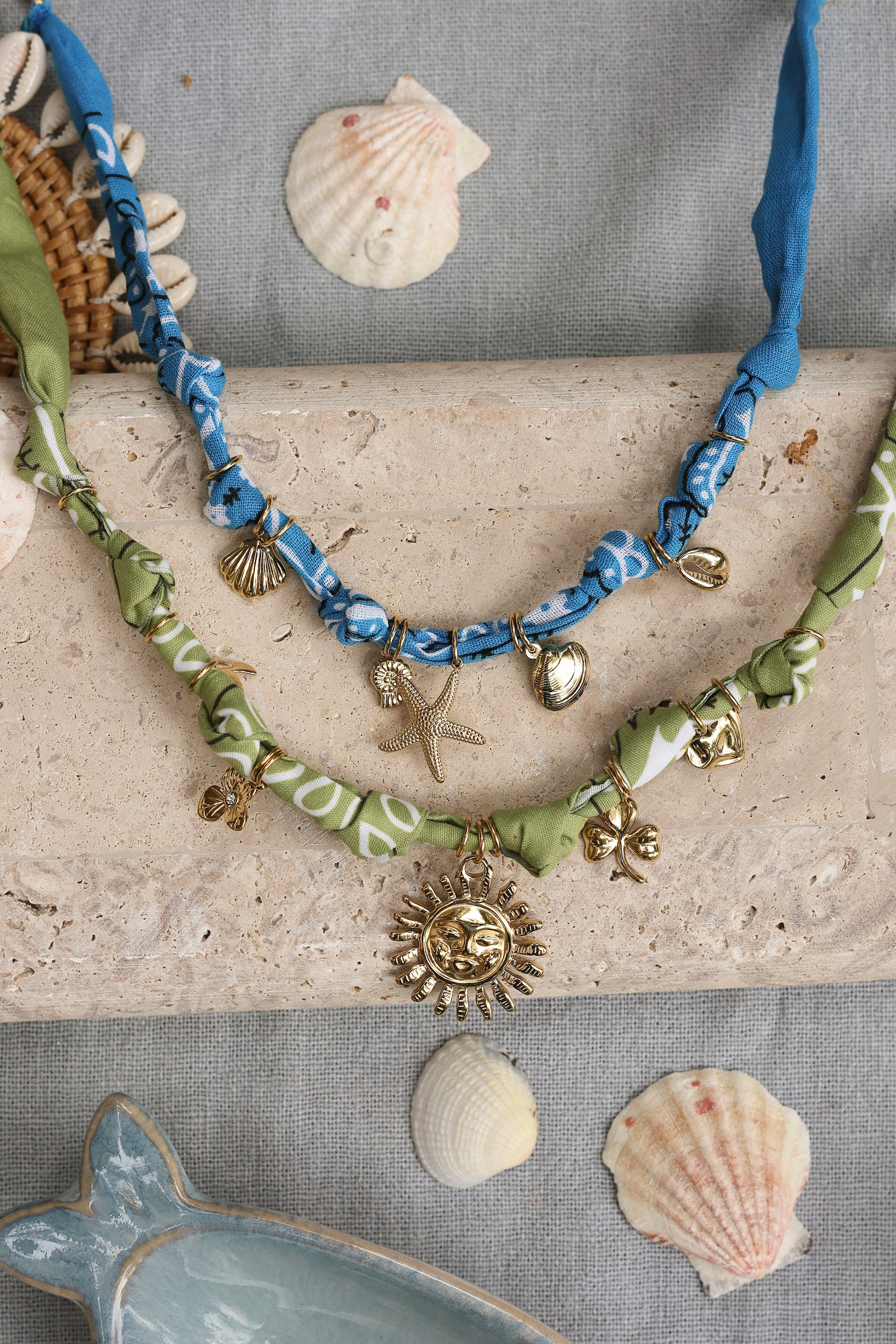 Collier doré Yarina vert tissu bandana vert avec pendentifs colibri, soleil, fleur ornée d'un zircon, trèfle et cœur - Bijou photographié dans un décor estival
