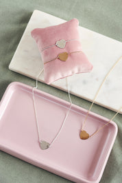 Collier personnalisable doré Adelie chaîne fine et médaille en forme de cœur à graver - Bijou photographié dans une coupole rose 