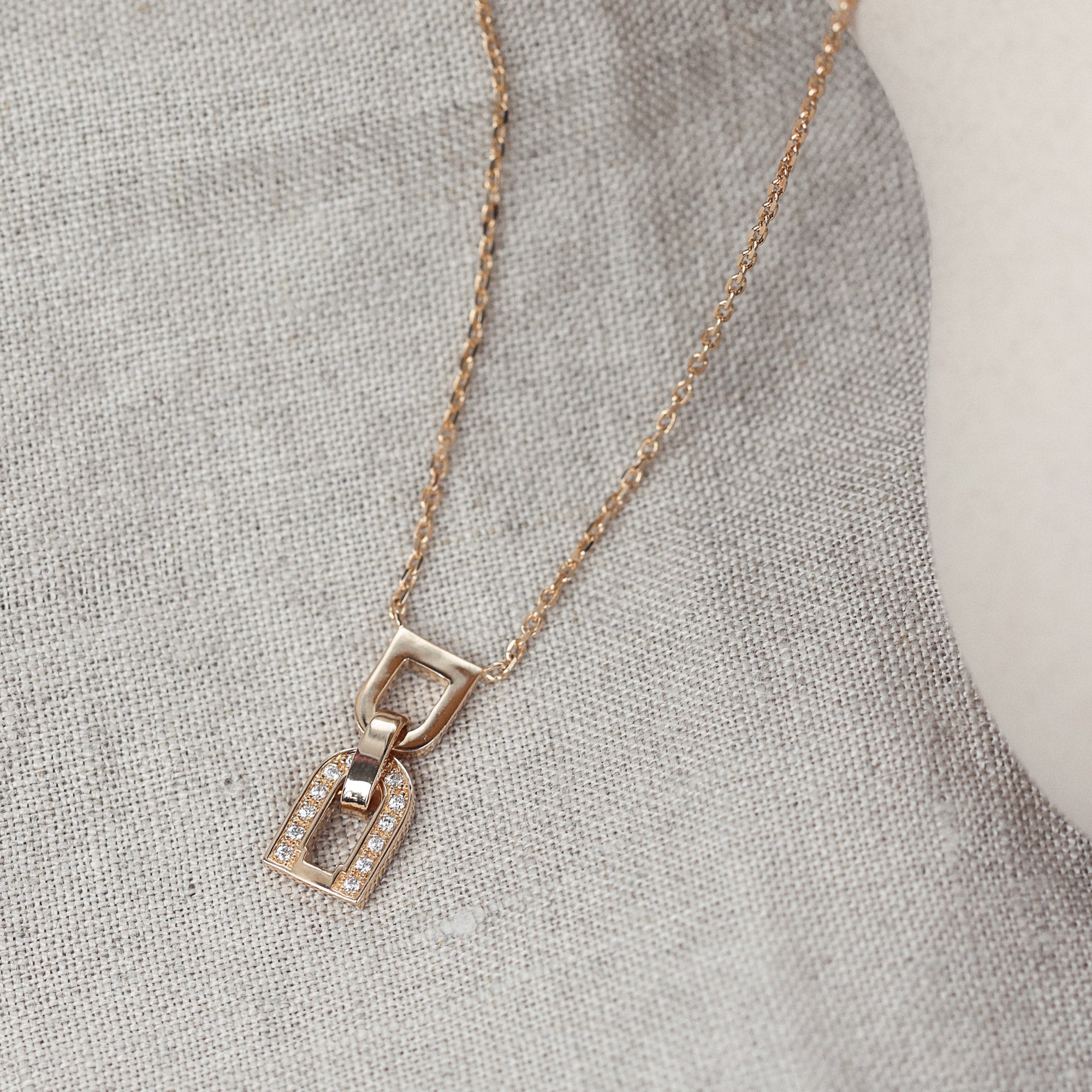 Collier doré Berny pendentif en forme de maille avec zircons - Bijou photographié sur tissu en lin
