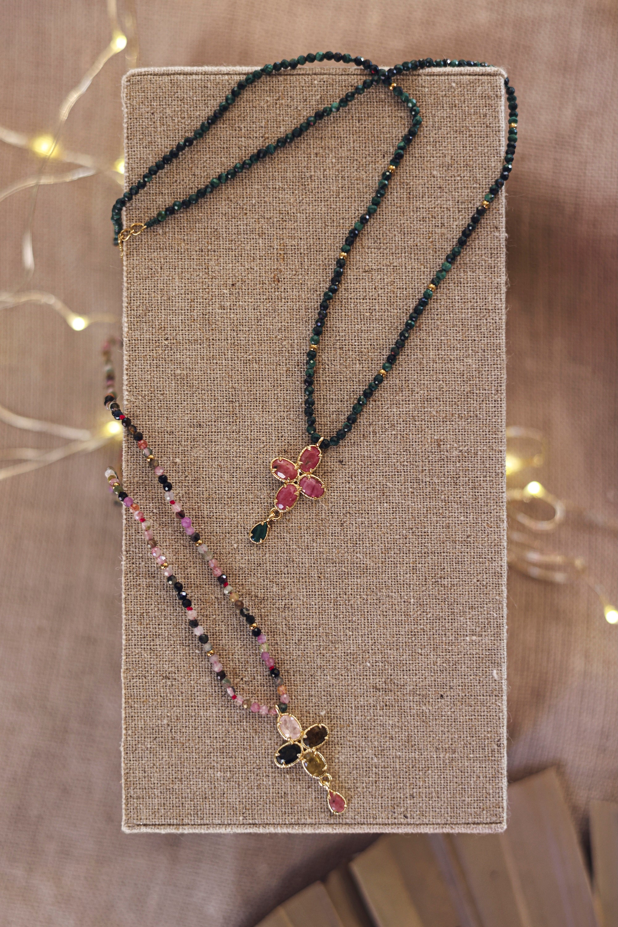Collier doré Kassya tourmaline avec pendentif fleur et pierres naturelles - Bijou photographié sur présentoir en lin gris avec des lumières en fond