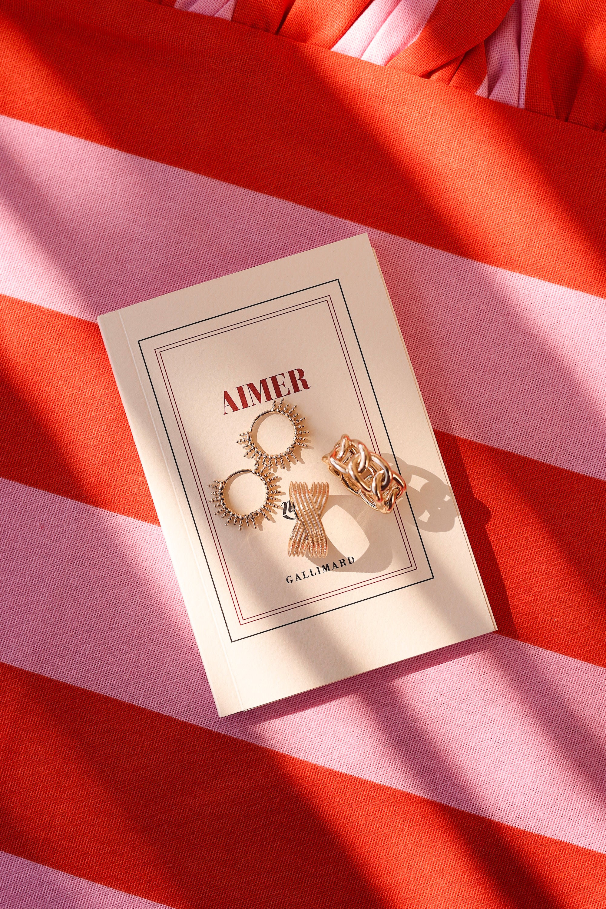 Boucles d'oreilles créoles dorée Adi soleil - Bijou photographié sur un livre "aimer" posé sur un tissu ligné rose et rouge.