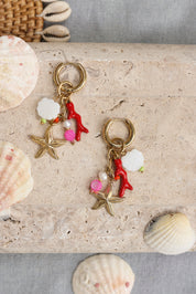 Mini créoles dorées Mirah corail pendentifs corail, étoile de mer, coquillage, perle en nacre, pierres colorées - Bijou photographié dans un décor estival