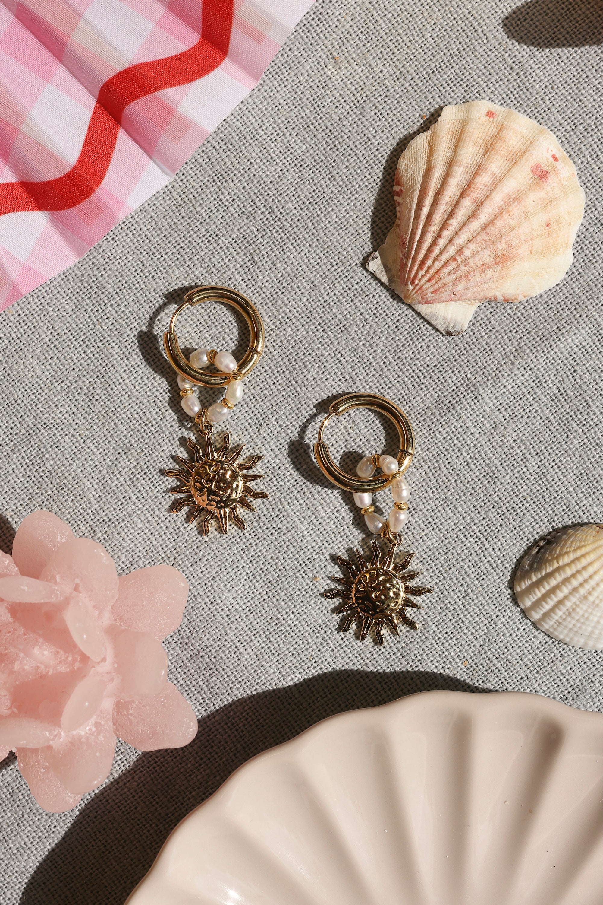 Boucles d'oreilles mini créoles dorées Zafira avec pendentif soleil et anneau orné de perles de nacre - Bijou photographié dans un décor estival
