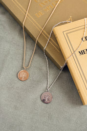 Médaille réversible en argent arbre de vie avec une face ornée d'un arbre de vie et une face lisse pour gravure - Bijou photographié sur un tissu kaki avec des livres